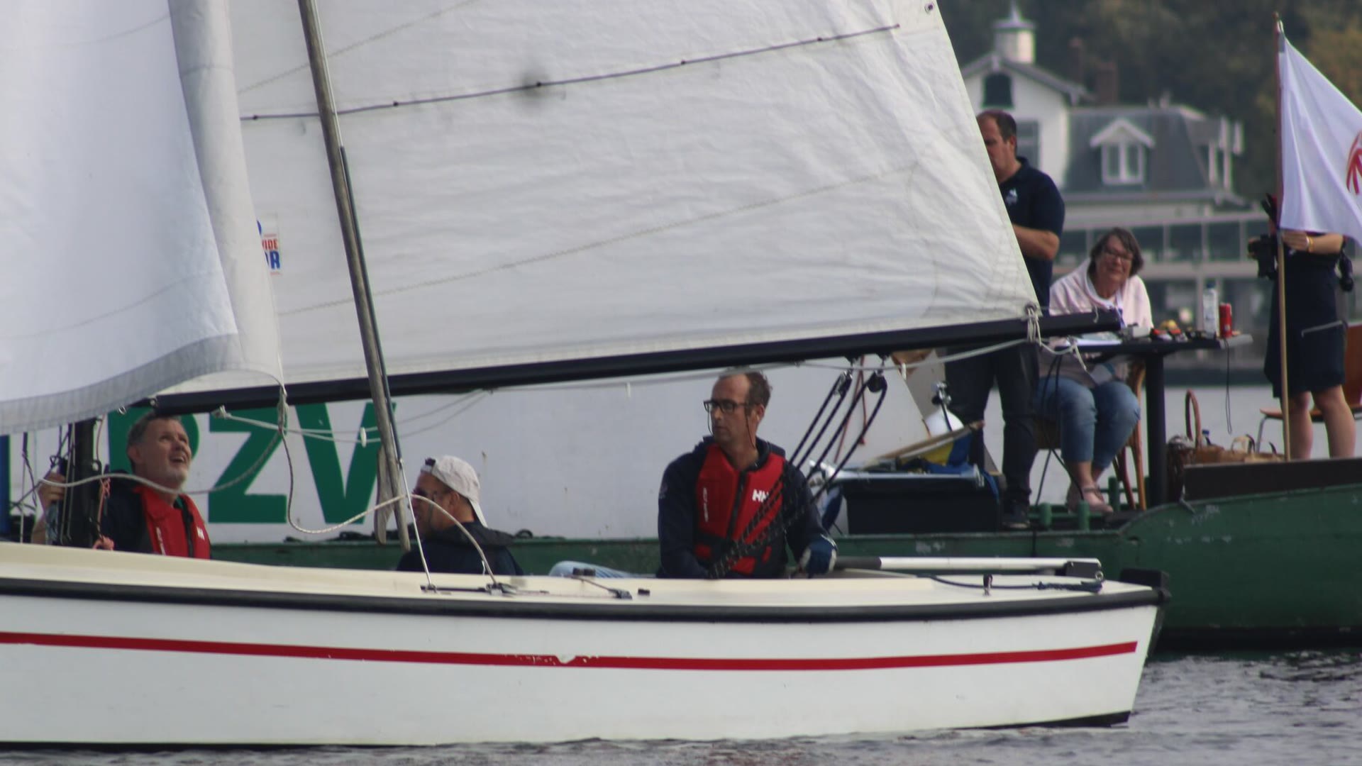 Een bemanning zeilt over de finishlijn langs de comitéboot, waar de wedstrijdleiding de finish klokt en de uitslag noteert.