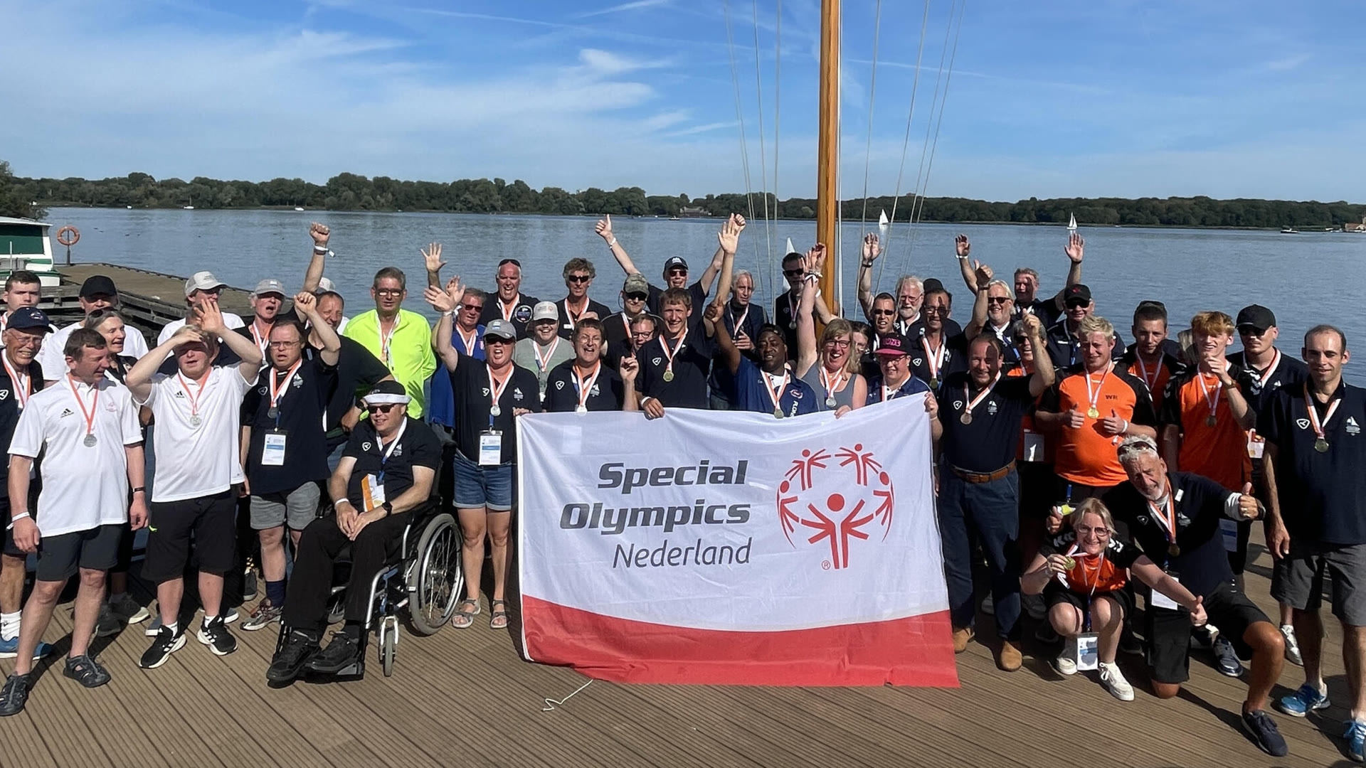 Zeilers, partners en vrijwilligers staan met hun medailles op de steiger voor een banier van Special Olympics Nederland.